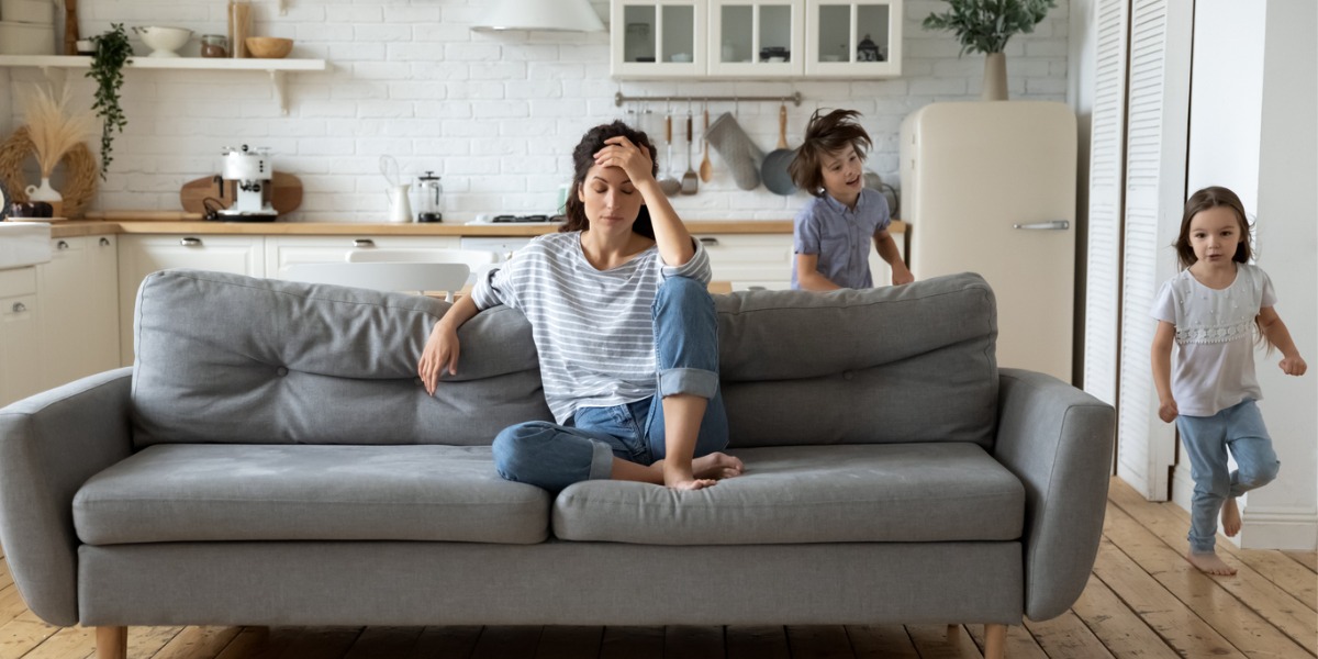 mother with depression sits on couch while children play