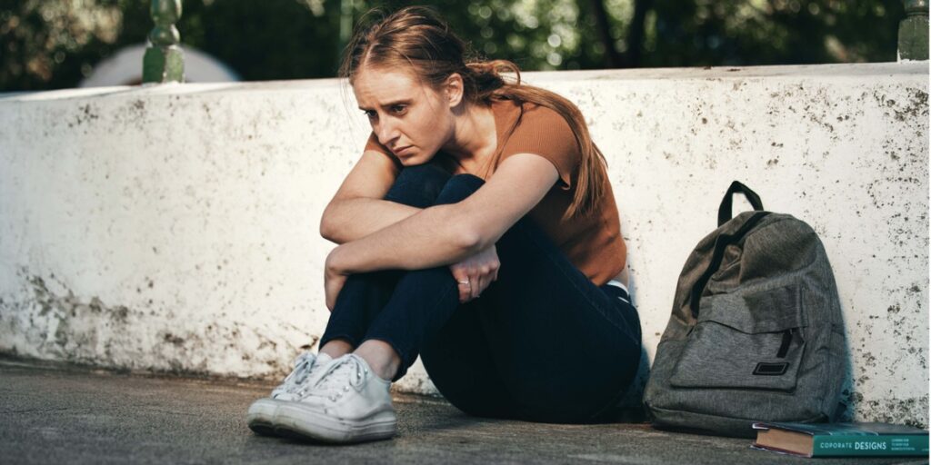 college young adult with anxiety sits by bookbag